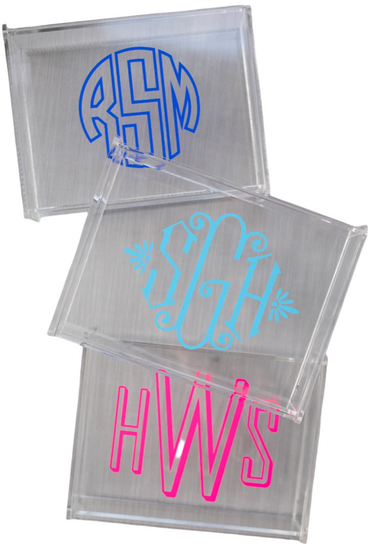 Clear acrylic blocks with monogrammed initials in blue, pink, and white on a metallic surface.